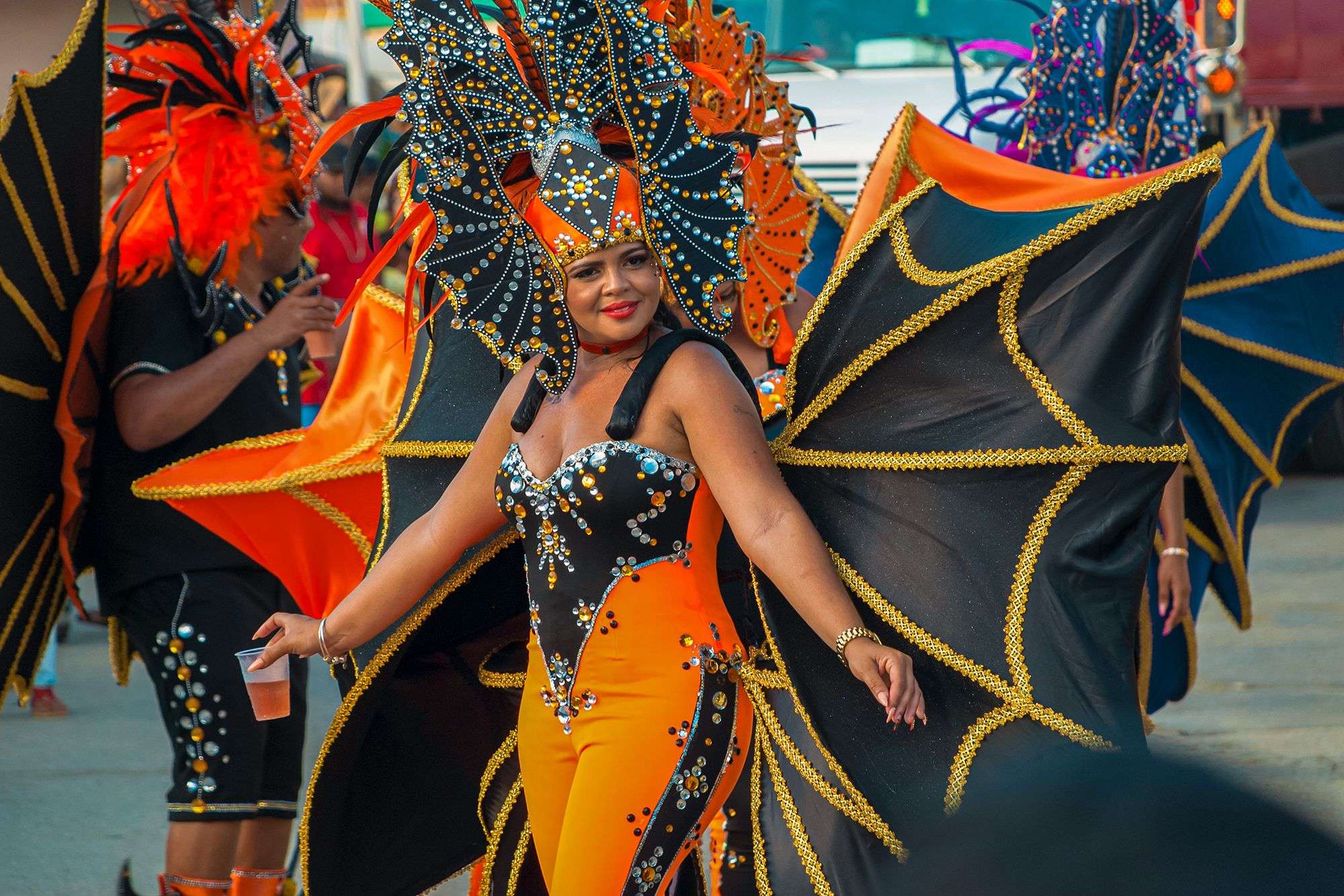 Beautiful woman in elaborate black and orange costume holding a cocktail as she walks in the Carnival parade in Curacao